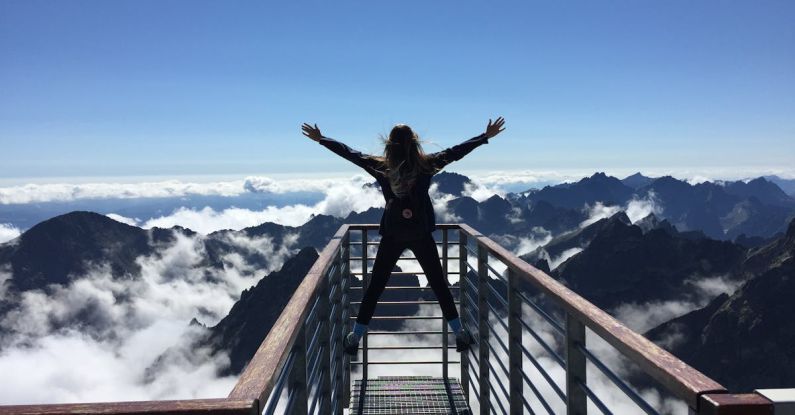 Origin Of Life - Person Standing on Hand Rails With Arms Wide Open Facing the Mountains and Clouds