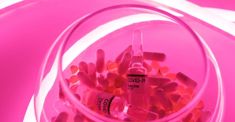Medical Inventions - From above of glass bowl filled with pills and ampoules with vaccine for COVID 19 in pink bright neon light